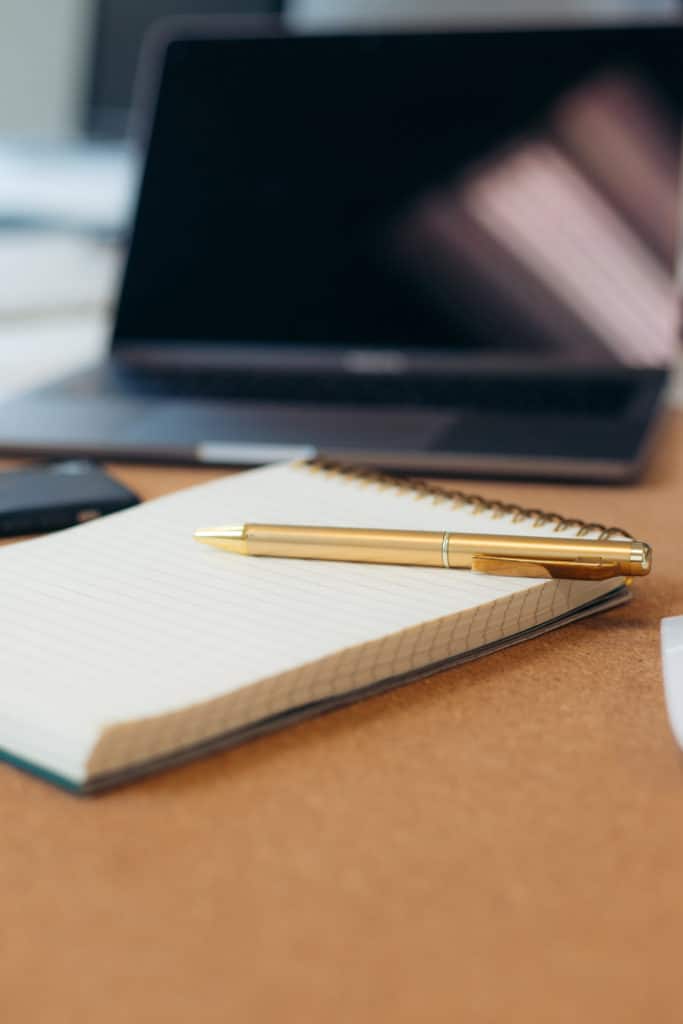 Gold pen sitting on a pad with a laptop in the background.