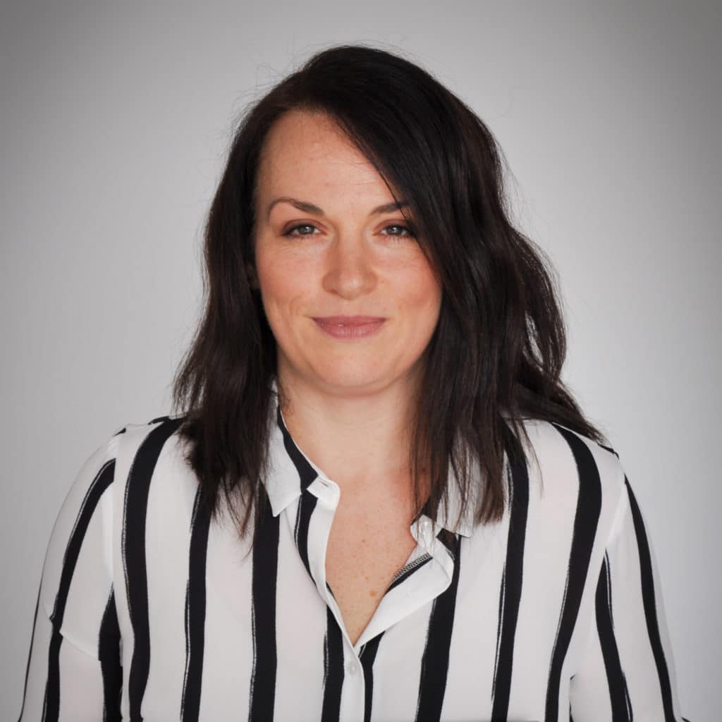 Rebecca Chivers smiling at the camera with a striped shirt on and plain background.