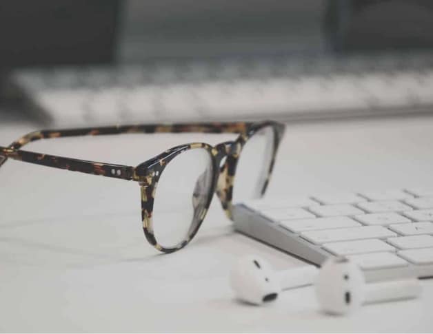 Photo showing glasses next to a keyboard with some ear buds